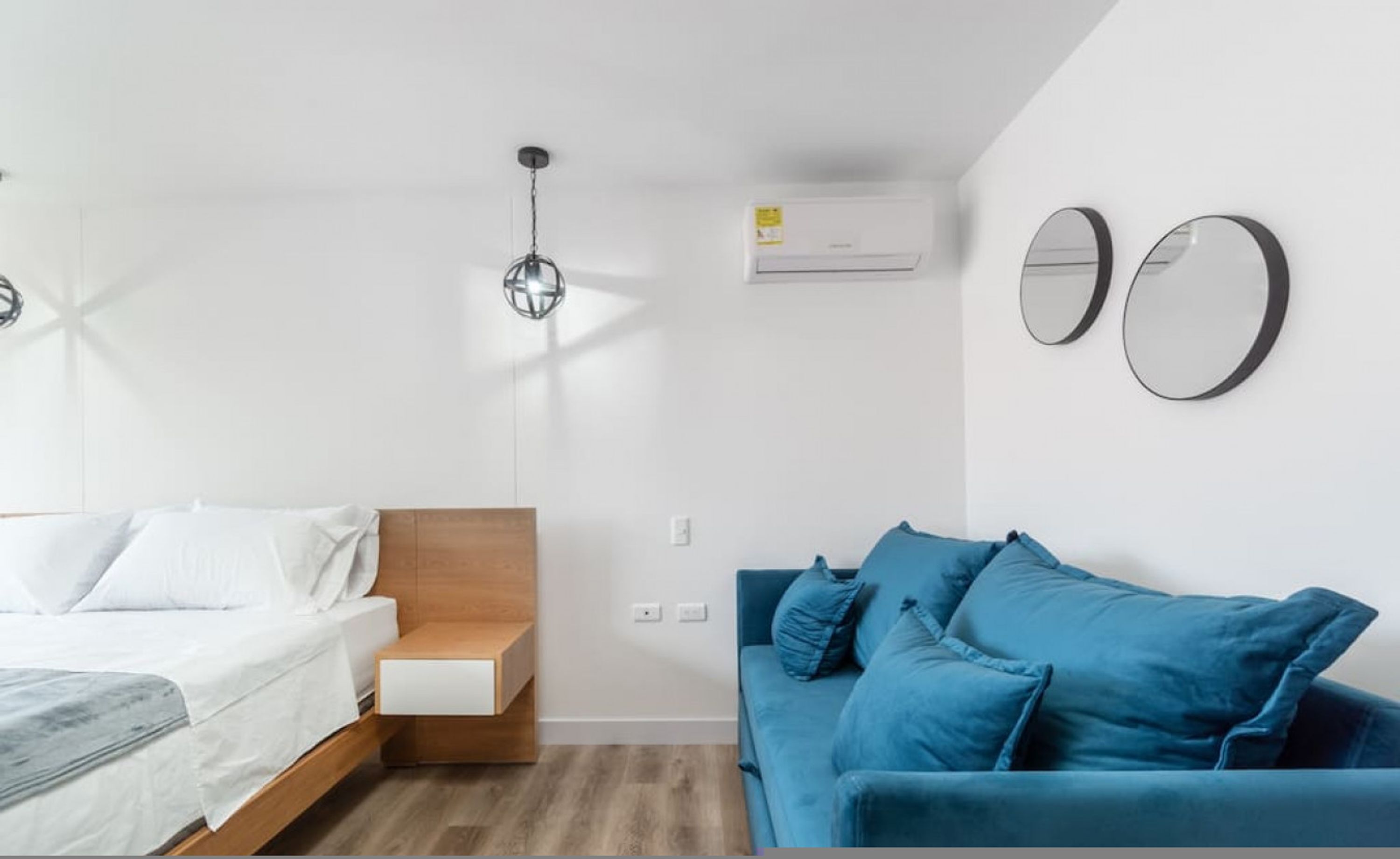 Un dormitorio con cama, mesita de noche y sofá azul con cojines.