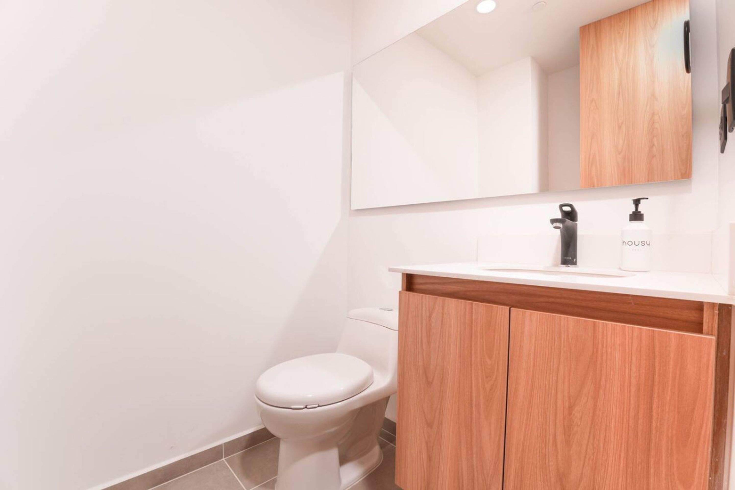 A modern bathroom with a white toilet, a wooden vanity, and a mirror above the sink.