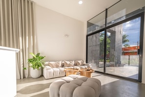A modern living room with a sofa, two wooden side tables, a large window, and a potted plant. - Metropolitan Living - 914 (Medellín)