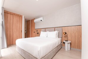 A modern bedroom with a large bed, wooden paneling on the walls, a round side table, and a ceiling-mounted air conditioning unit. - Metropolitan Living - 914 (Medellín)