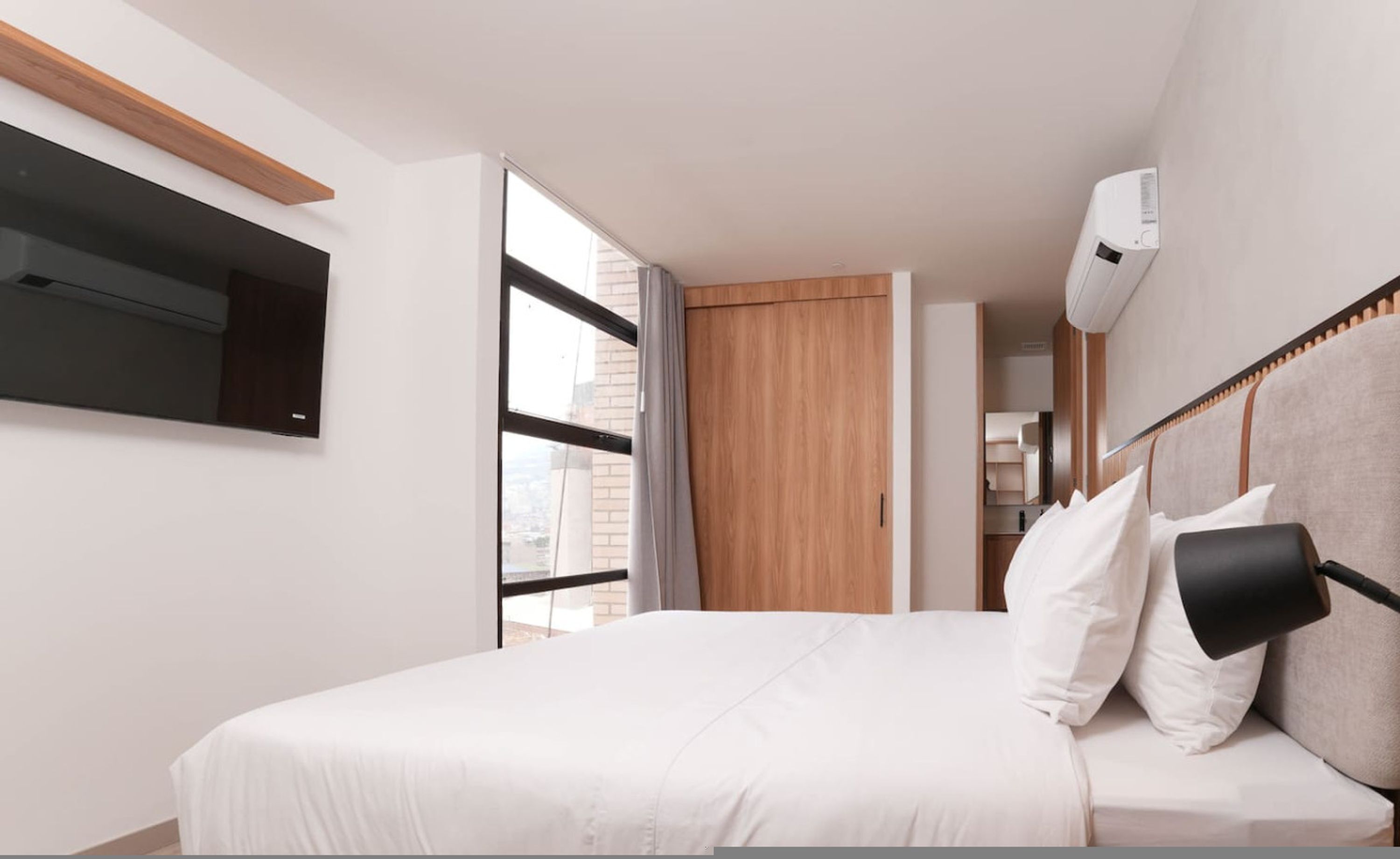 A modern hotel room with a bed, a TV mounted on the wall, and a window with curtains.