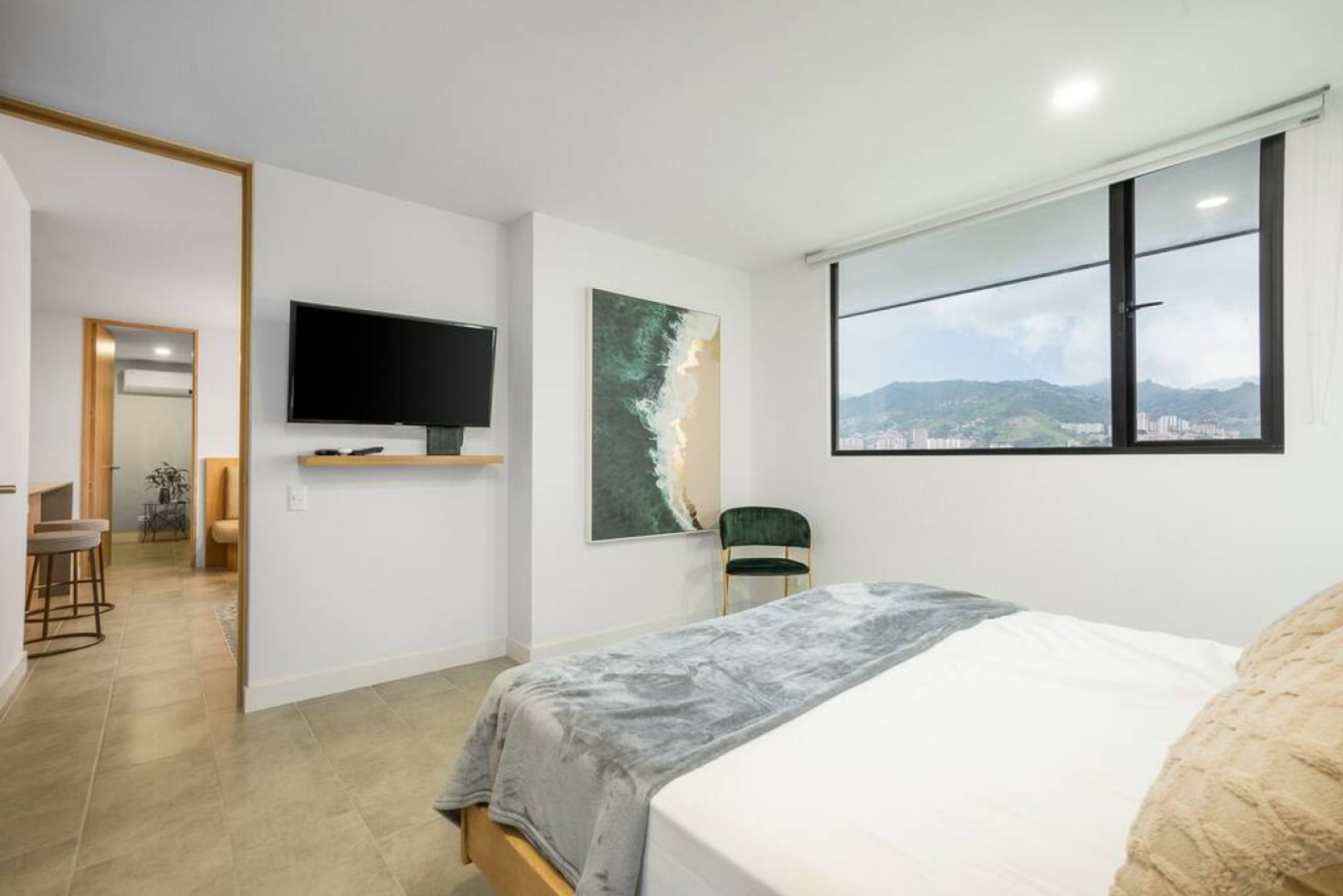 Une chambre à coucher avec un lit, une télévision, un tableau et une fenêtre donnant sur la ville.