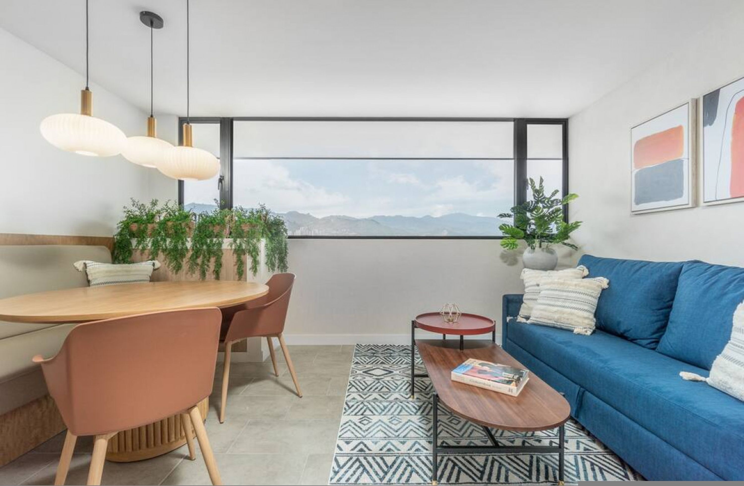 A modern living room with a dining area, a blue sofa, and a view of mountains through a large window.