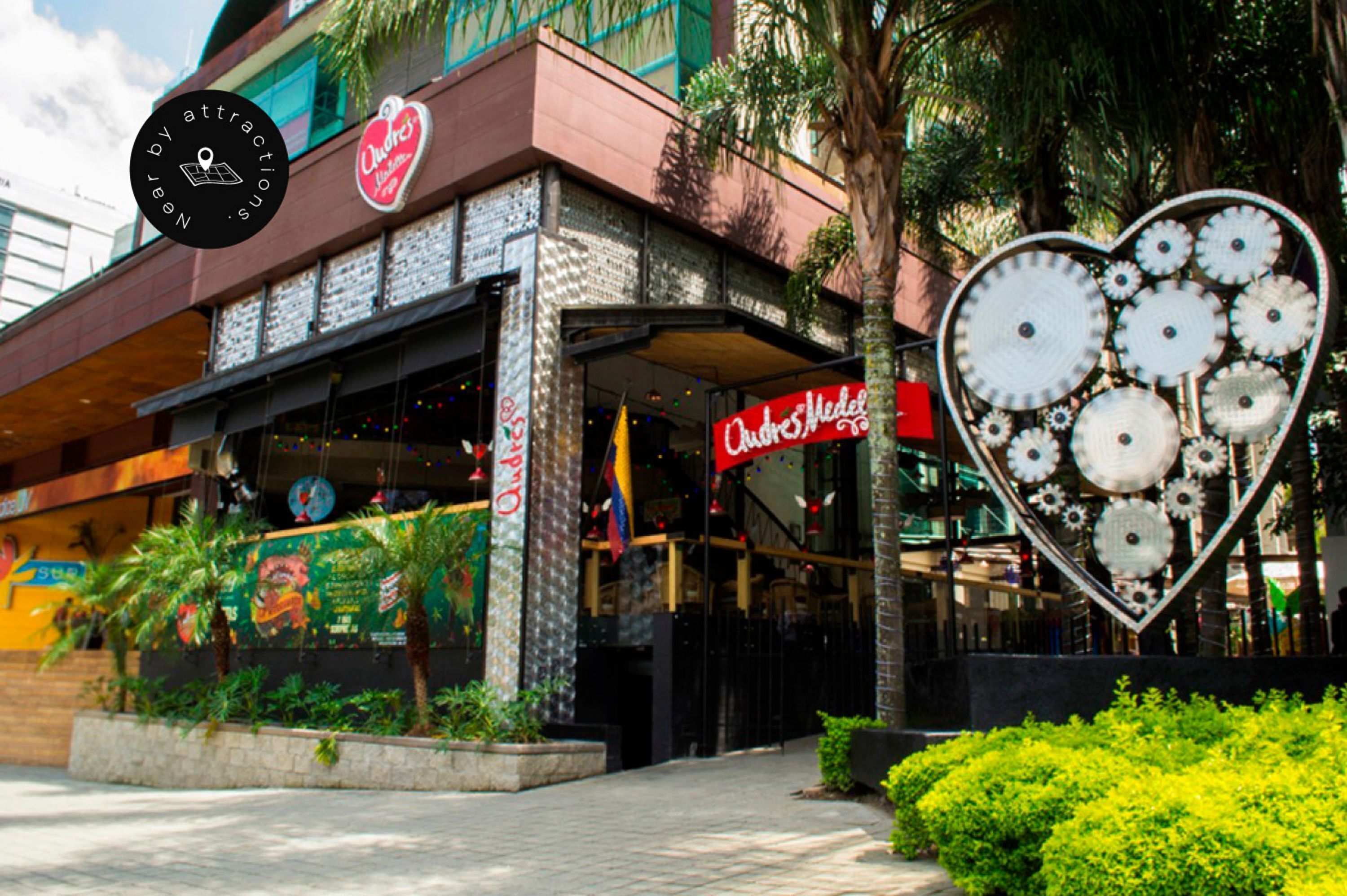 A building with a heart-shaped sculpture in front, a sign for 'Ode's Medellin,' and a mural on the wall.