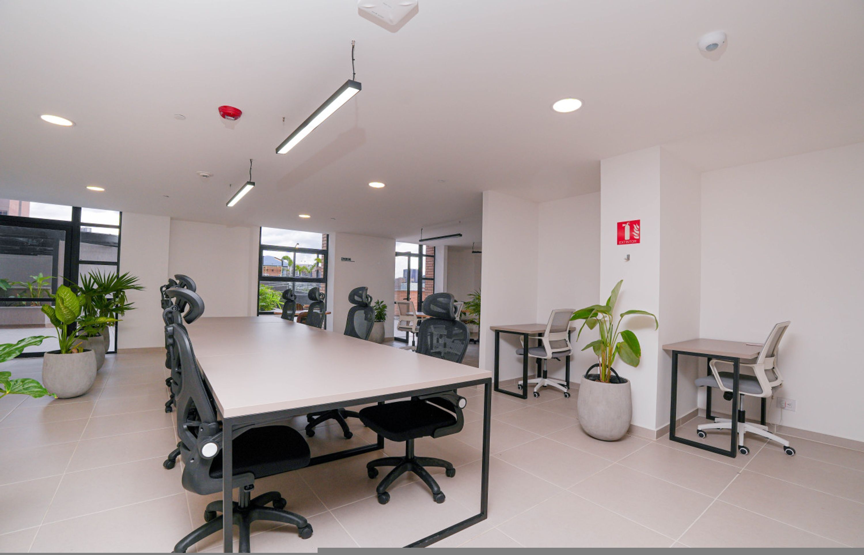 Uma sala de conferência com uma mesa comprida, várias cadeiras de escritório, plantas em vasos e um aviso de alarme de incêndio.