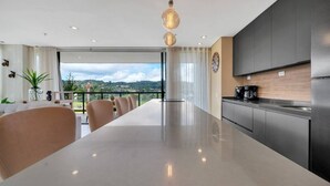 A modern kitchen with a long countertop, a dining area with chairs, and a view of the outdoors. - Olive Country Living - 301 (Envigado)