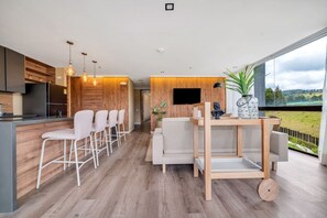 A modern kitchen with wooden accents, a dining area with a sofa, and a large window with a view. - Olive Country Living - 301 (Envigado)