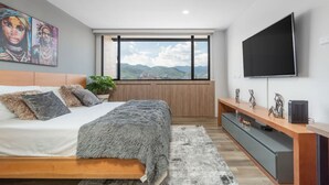 A bedroom with a bed, a TV, a window with a mountain view, and a plant. - Go Living Suites - 1219 (Medellín)