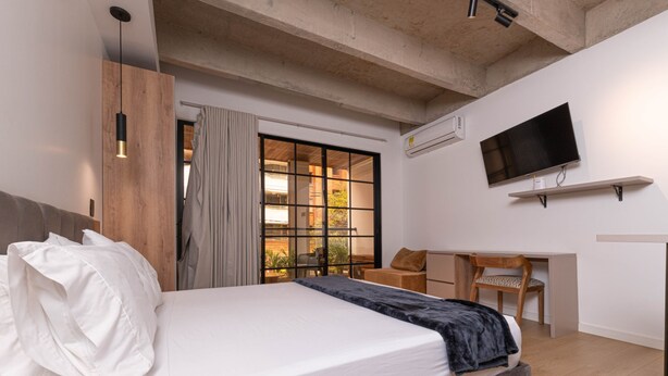 A modern bedroom with a bed, a desk, a chair, a TV, and a window with curtains. - Opera 503 in Medell n (Medellín)