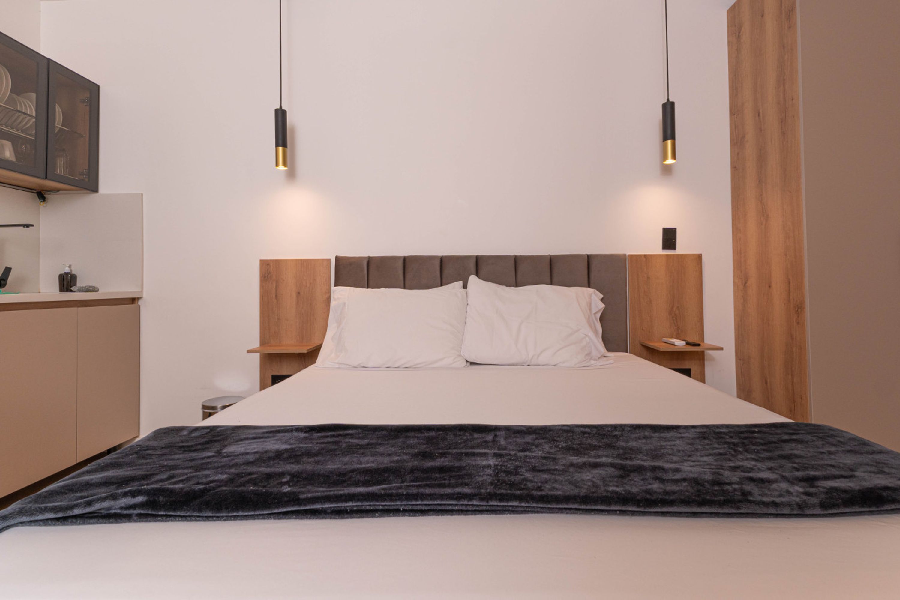 A bedroom with a bed, wooden headboard, bedside tables, and pendant lights.