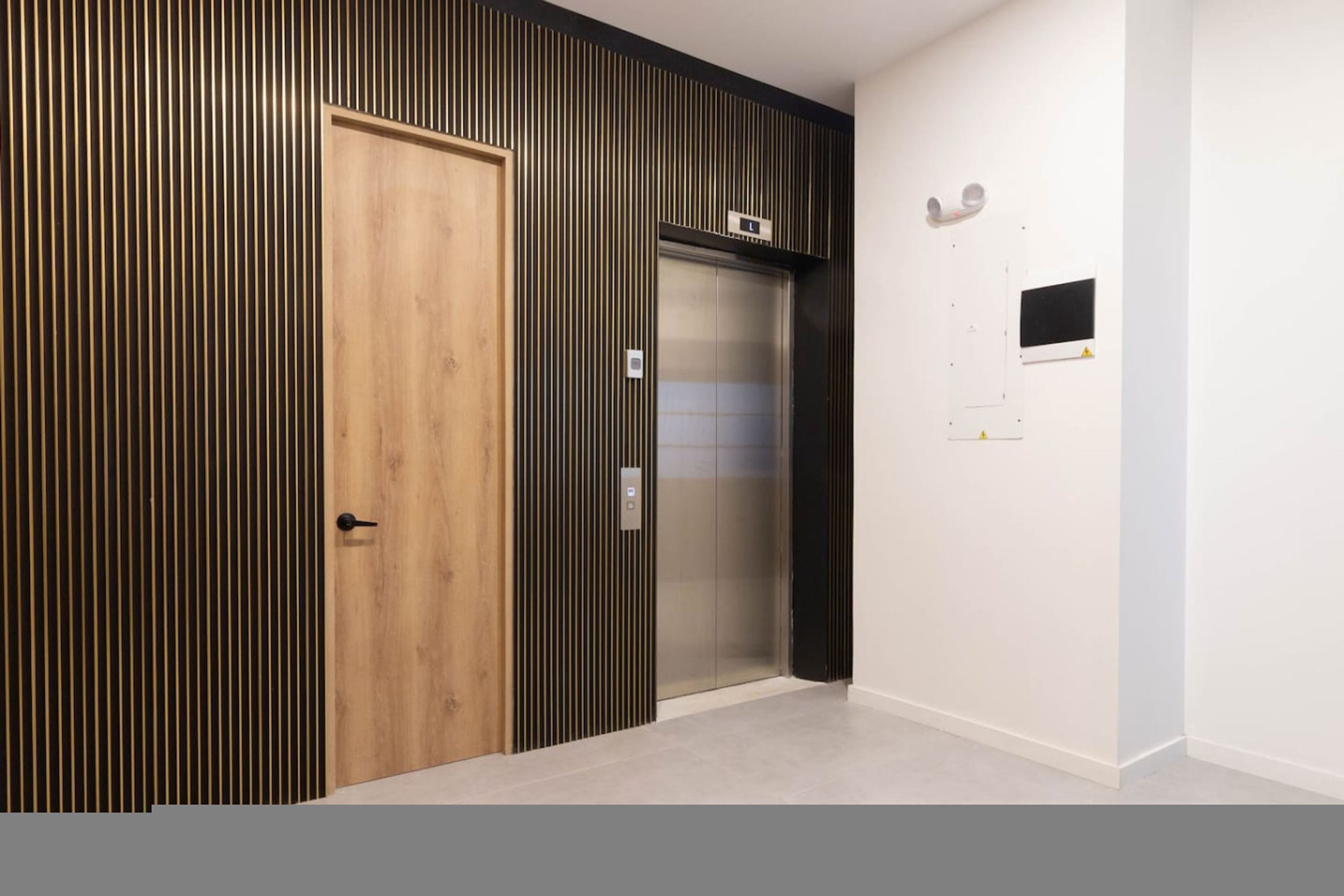 A modern elevator with a metallic finish, a wooden door, and a wall-mounted control panel.