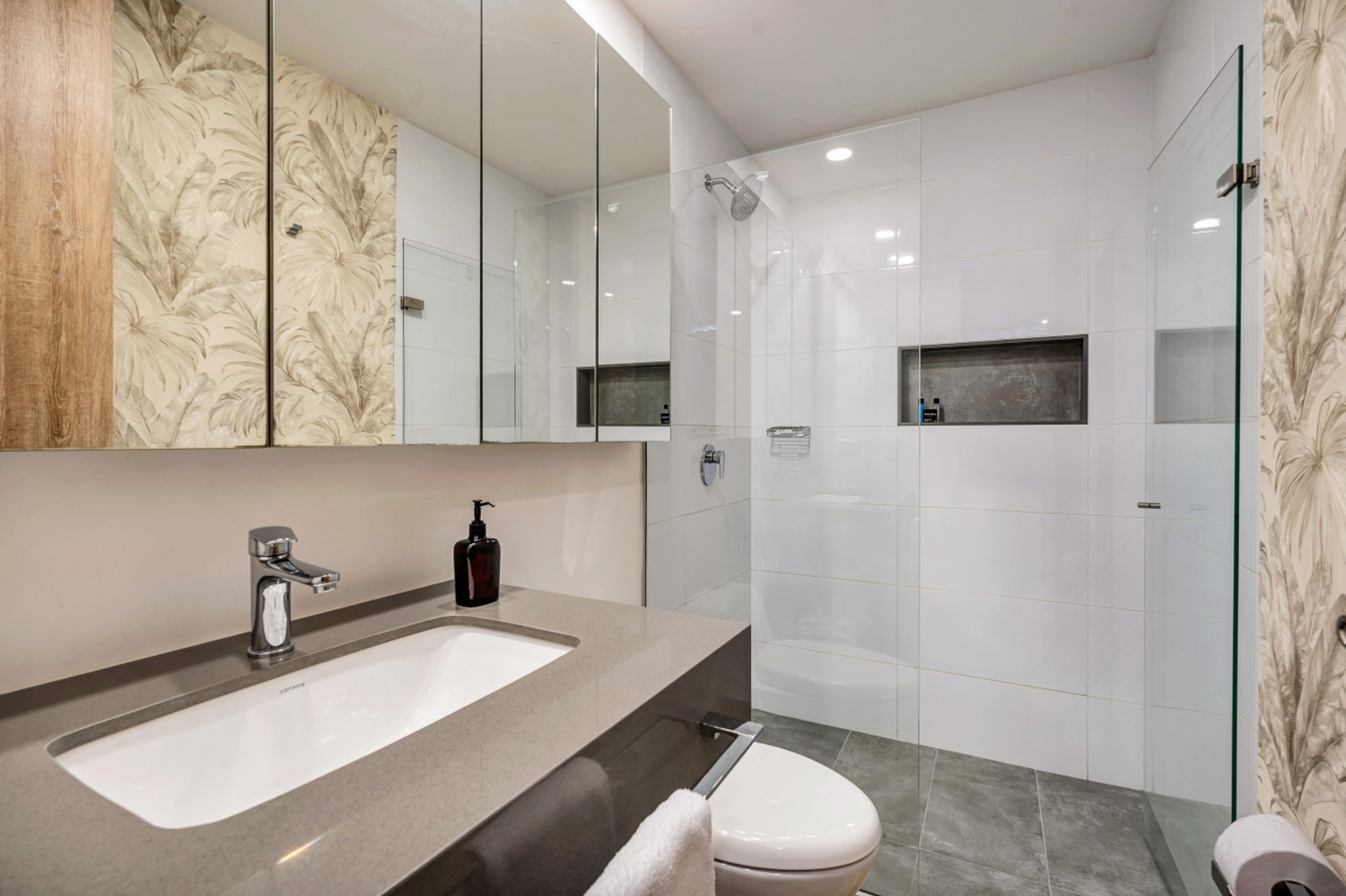 A modern bathroom with a large mirror, a sink, a toilet, and a shower area.