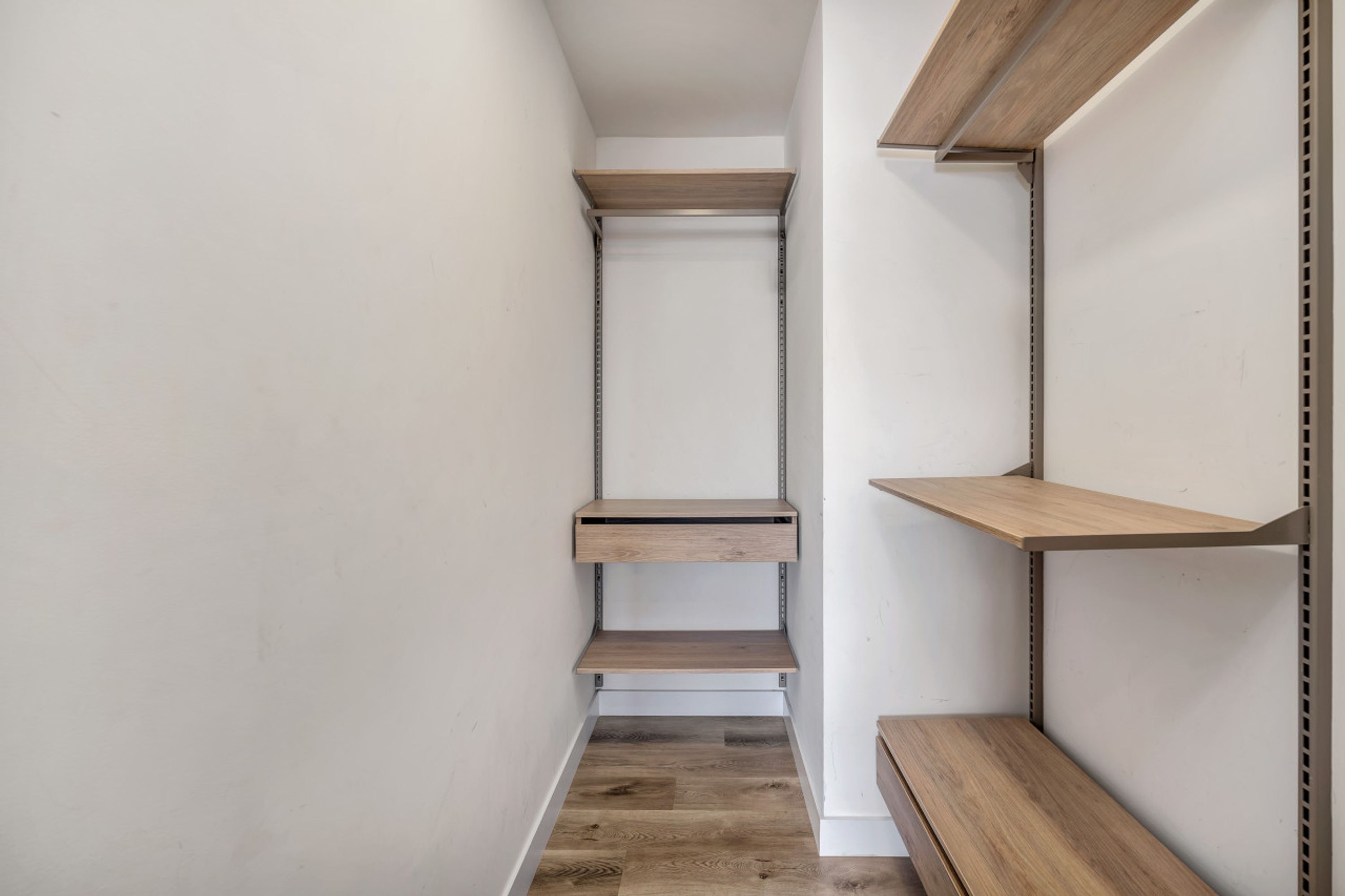 A narrow hallway with wooden shelves and a white wall.