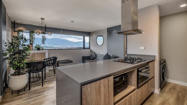 A modern kitchen with a large island, built-in oven, and a view of mountains. - Go Living Suites - 801 (Medellín)