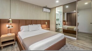 A modern hotel room with a large bed, bedside lamps, a mirror, and an air conditioning unit. - Go Living Suites - 801 (Medellín)