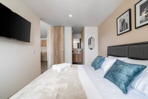 Une chambre d’hôtel équipée d’un lit, d’un téléviseur à écran plat, d’un miroir et de tableaux encadrés au mur.