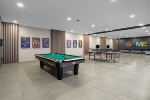 Une salle de billard équipée d’une table de billard, d’une table de ping-pong et de plusieurs affiches murales.