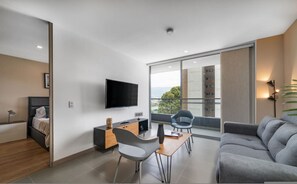 Un salon moderne doté d’un téléviseur à écran plat, d’un canapé, d’une table à manger avec des chaises et d’un balcon offrant une vue agréable.