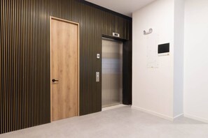 A hallway with a wooden door, a vertical striped wall, an elevator, and a white wall with a small black panel. - Opera 204 in Medell n (Medellín)