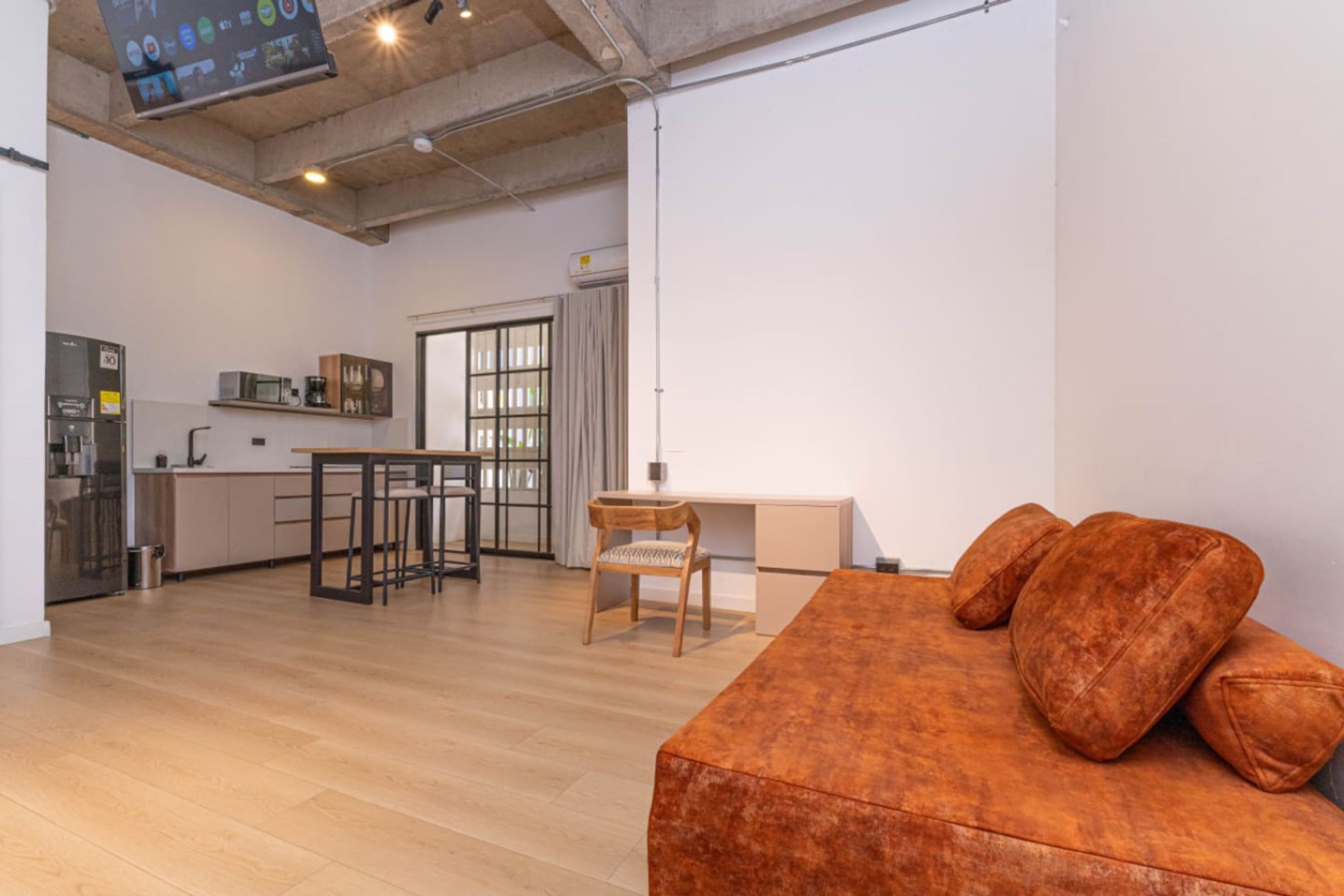 Un interior moderno con suelo de madera, un sofá con cojines, un comedor con sillas y una cocina equipada.