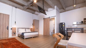 Moderni hotellihuone, jossa on sänky, työpöytä, tuoli ja pieni keittiönurkkaus.