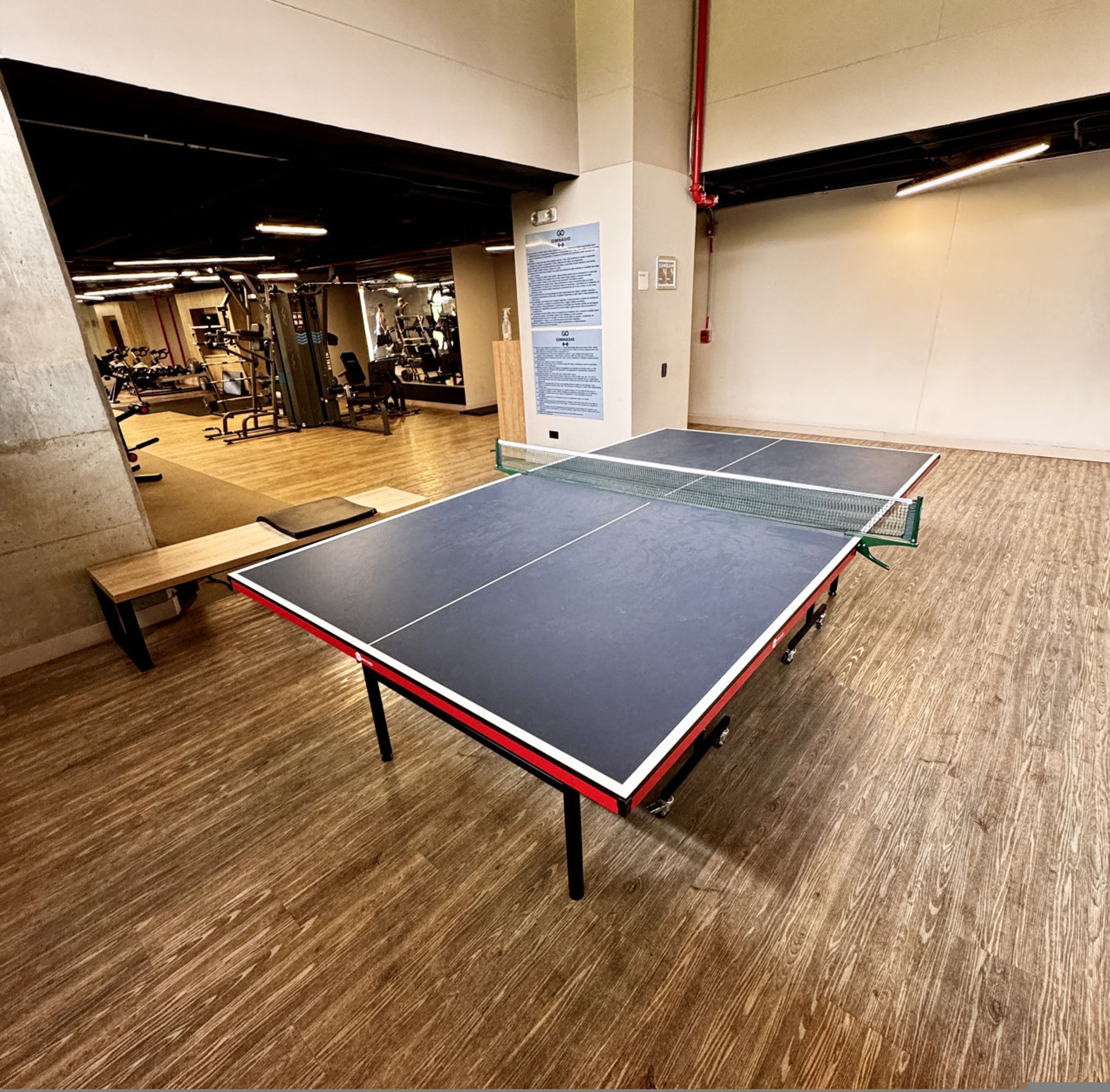 A ping pong table in a gym with wooden flooring, exercise equipment, and a bench.