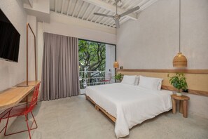 A bedroom with a bed, a desk, a chair, a ceiling fan, a window with curtains, and a view of trees. - Botánica 307-deluxe (Medellín)