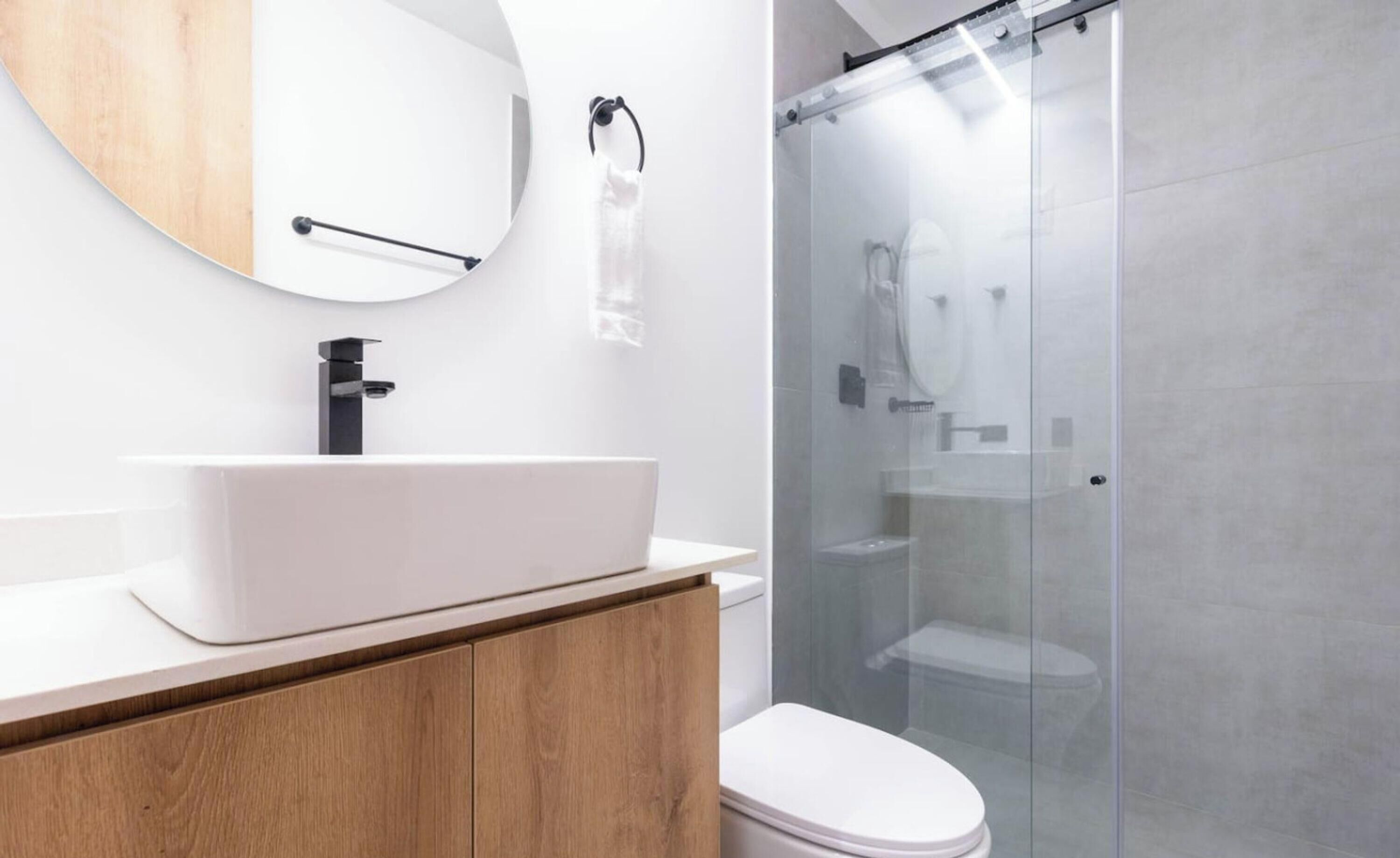 A modern bathroom with a white sink, wooden vanity, and a glass shower enclosure.