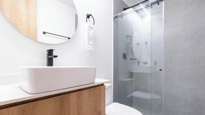 Un baño moderno con un lavamanos blanco, tocador de madera y cabina de ducha de vidrio.