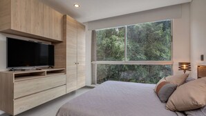 A bedroom with a bed, a TV, wooden cabinetry, and a large window with a forest view. - Oslo 603 B in Medell n (Medellín)