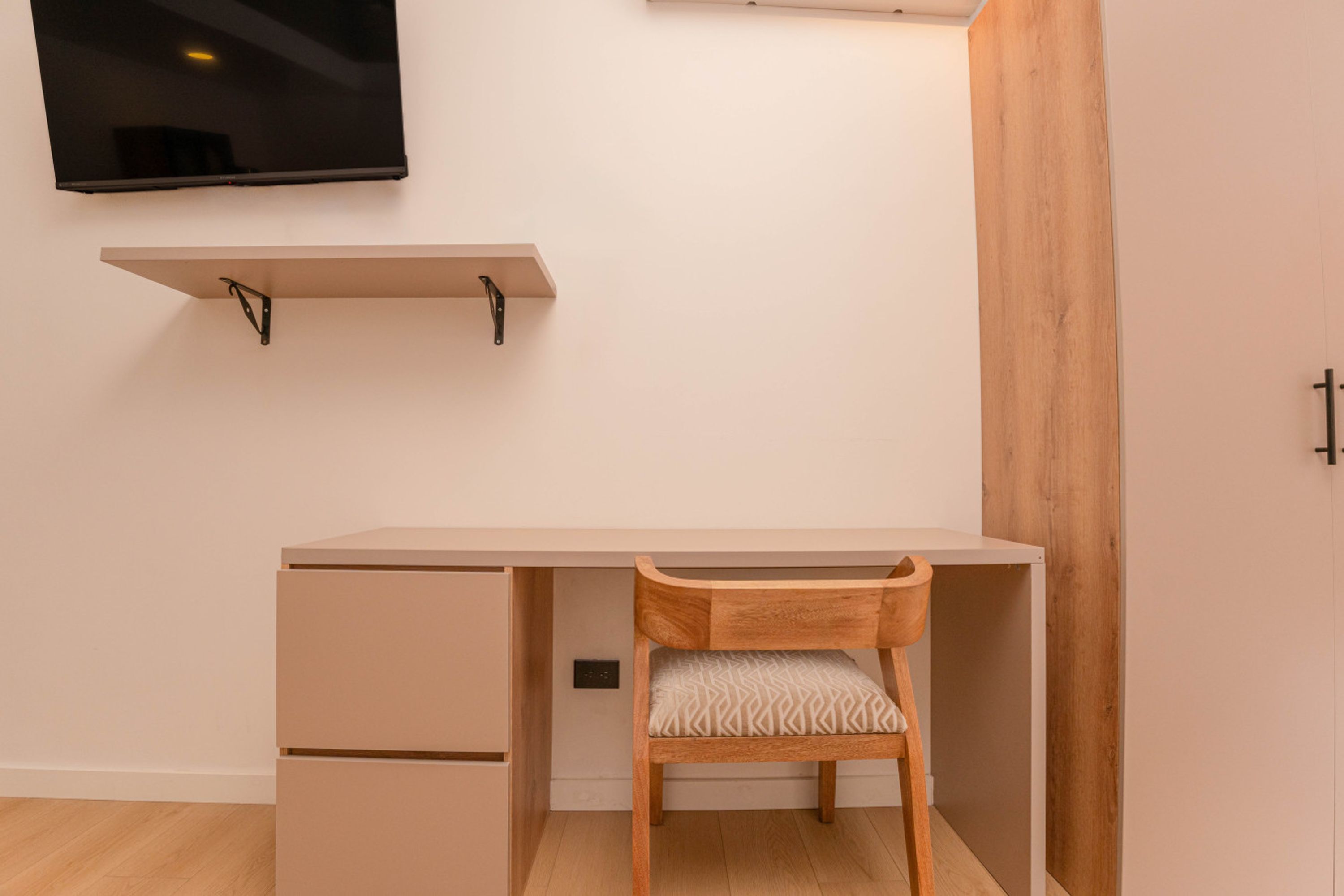 Een moderne kamer met een houten bureau, een stoel, een aan de muur bevestigde televisie en een houten paneel.