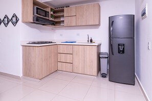 Una cocina moderna con armarios de madera, microondas integrado, refrigerador de acero inoxidable y estufa a gas.