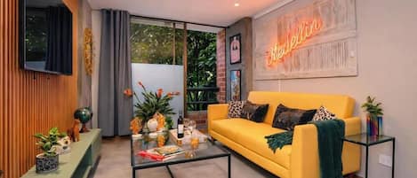 Un salon moderne avec un canapé jaune, une table basse en verre et un néon mural.