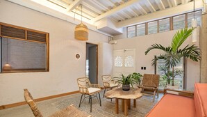 A room with wicker furniture, a round wooden table, and a large window with blinds. - Botánica Básica (Medellín)