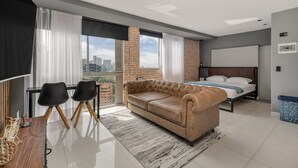 A modern bedroom with a large bed, a sofa, a desk with chairs, and a view of the city. - Oslo 2101 in Medell n (Medellín)