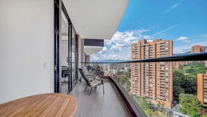 Ein Balkon mit Holztisch und -stühlen, einer Glastür und Blick auf die Stadt.
