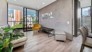 Ein modernes Wohnzimmer mit einer Couch, einem kleinen Tisch, einem Sessel und Blick auf eine Stadtlandschaft durch große Fenster.