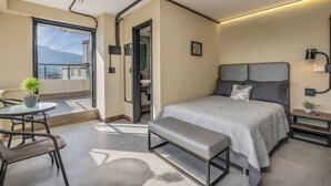 Un dormitorio moderno con una cama grande, una pequeña mesa con sillas, un banco y vistas al exterior.
