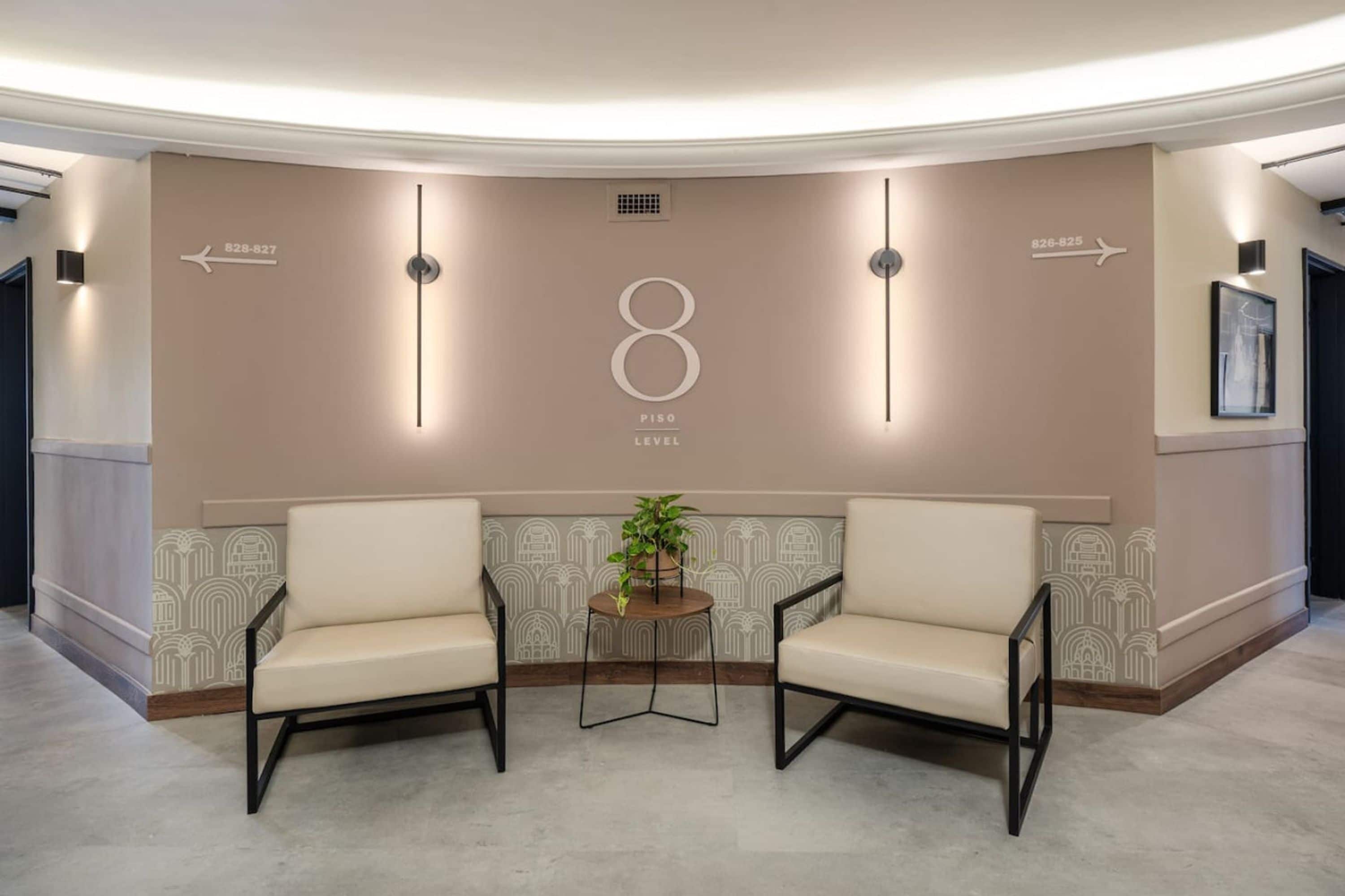 A lobby with two chairs, a small table with a plant, and a wall with directional arrows and a large number '8'.