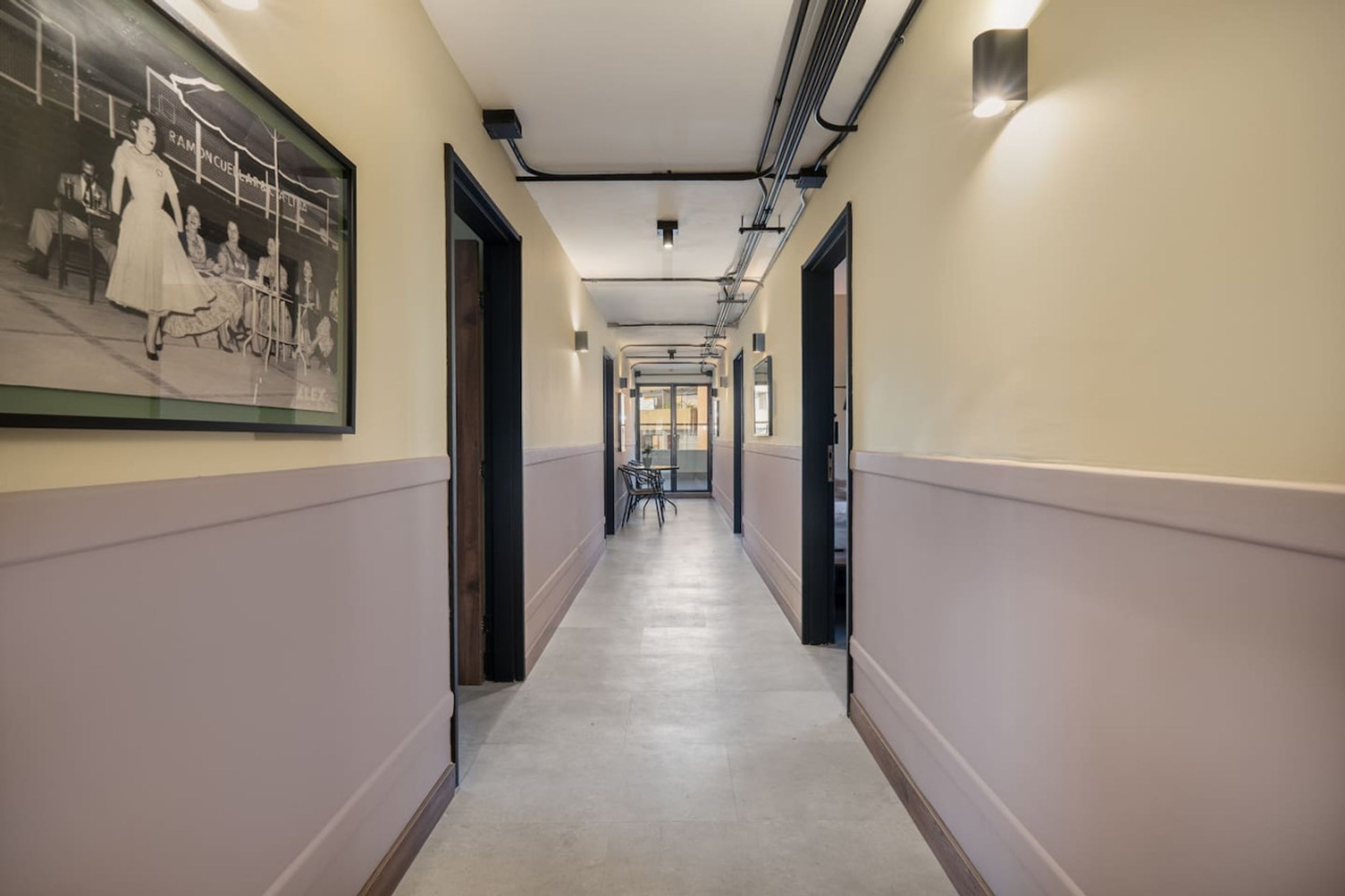 A hallway with a framed historical photo, doors on both sides, and a tiled floor.