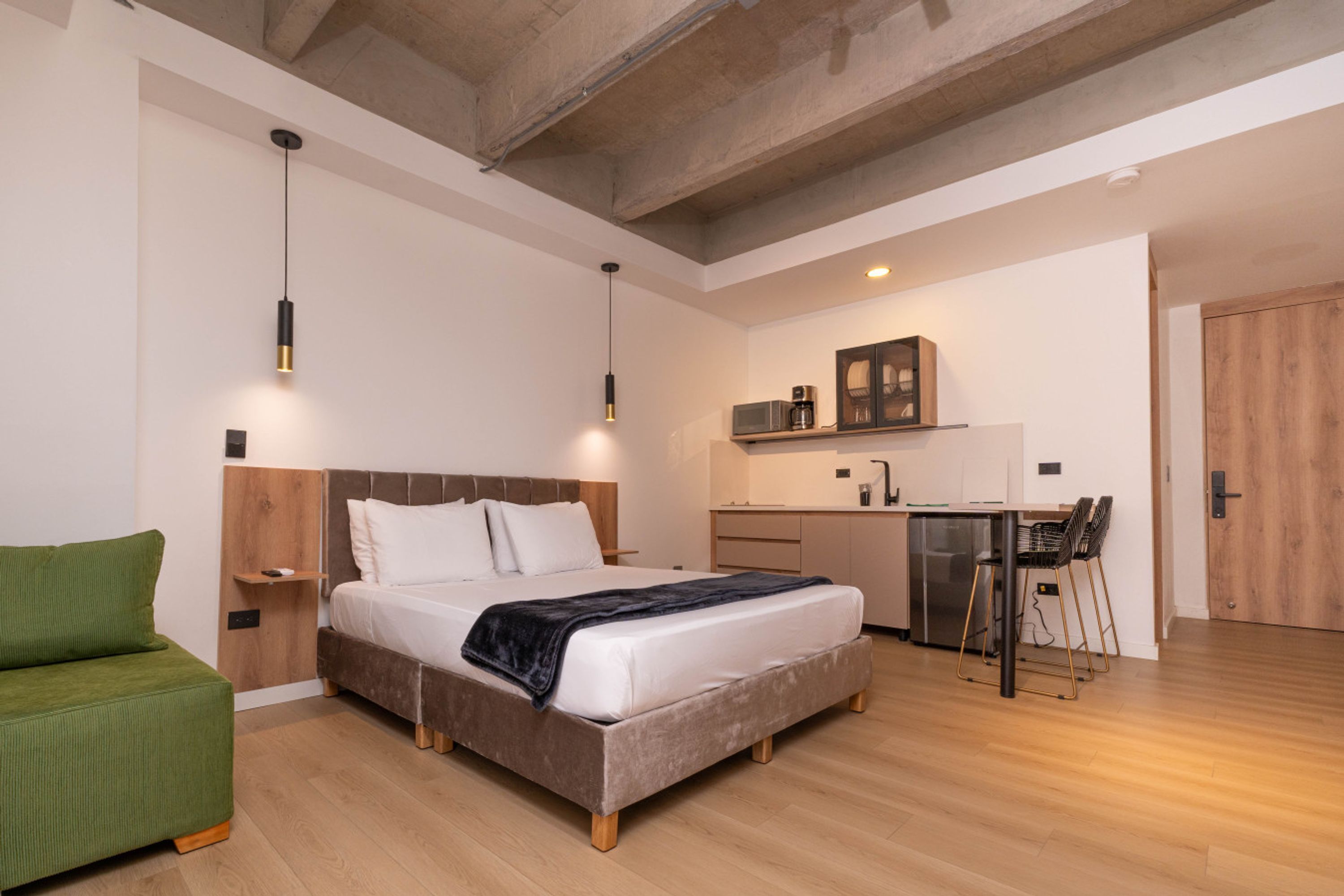 A modern room with a bed, a green chair, a kitchenette, and a wooden door.