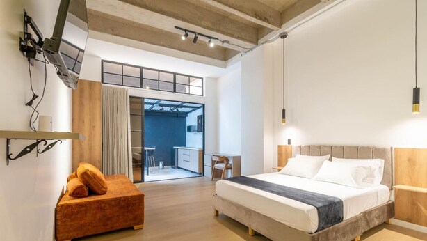 A modern bedroom with a bed, a wooden bench, a desk, and a view of the kitchen. - Opera 101 in Medell n (Medellín)