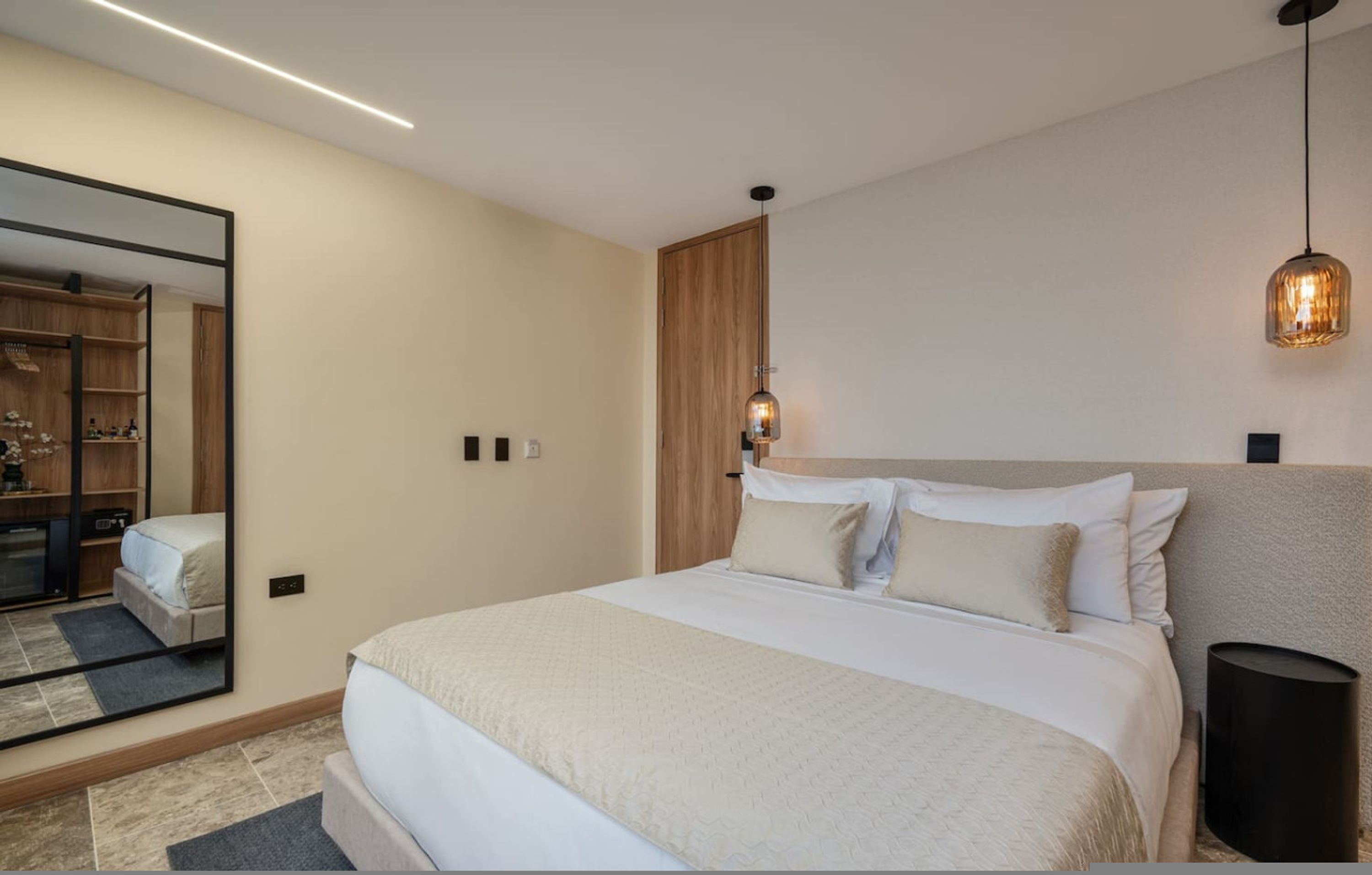 Une chambre moderne avec un grand lit, un miroir, une armoire et un luminaire suspendu.