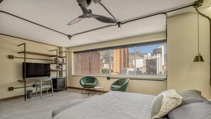 Ein modernes Hotelzimmer mit einem Bett, einem Schreibtisch, einem Sessel, einem Fernseher und einem großen Fenster mit Blick auf die Stadt.