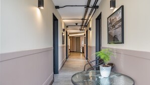 A hallway with a round table and potted plant, a framed picture on the wall, and exposed ceiling pipes. - Nutibara Express - 825 (Medellín)