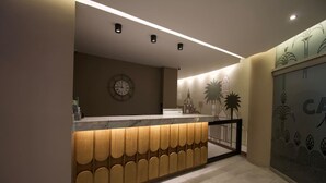 A reception desk with a clock, a wall with a floral pattern, and a staircase. - Nutibara Express - 825 (Medellín)