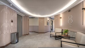 A modern lobby with a curved ceiling, a seating area with a sofa and chairs, directional signs, and a trash bin. - Nutibara Express - 825 (Medellín)