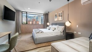 A modern hotel room with a large bed, a desk, and a TV. - Go Living Suites - 1111 (Medellín)