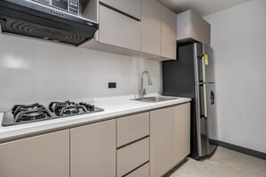 A modern kitchen with a gas stove, stainless steel refrigerator, and beige cabinetry. - Housy Laureles - 202 (Medellín)