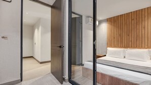 A modern bedroom with a glass door leading to a hallway, a wooden headboard, and a bed with white bedding. - Housy Laureles - 202 (Medellín)